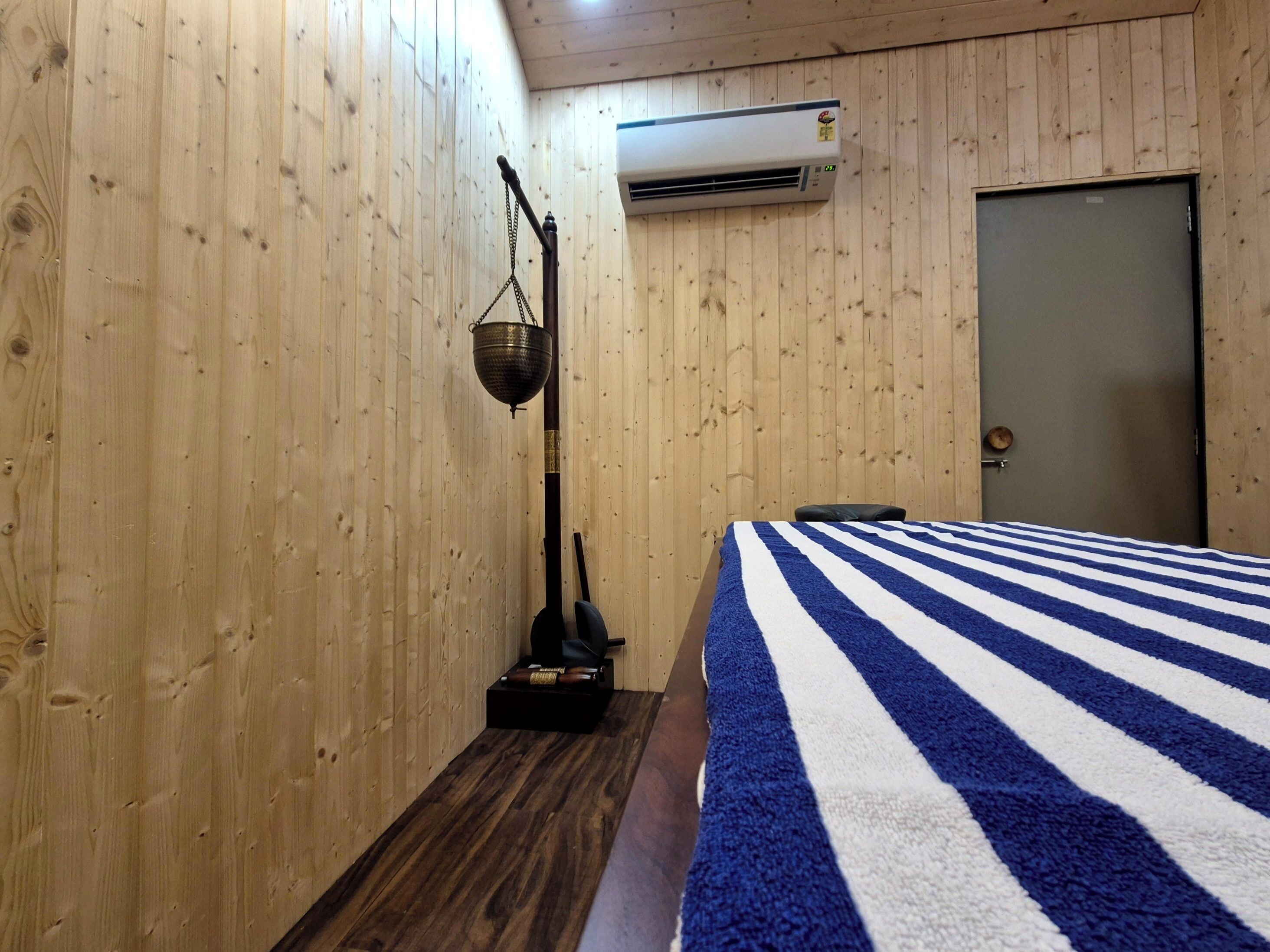 A room with wooden walls, a bed with a striped blanket, a hanging lamp, and an air conditioning unit.