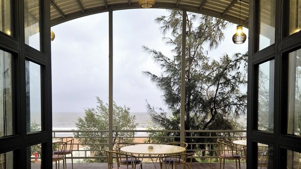 Una terraza abierta con una mesa redonda y sillas, con vistas a un cuerpo de agua y árboles.