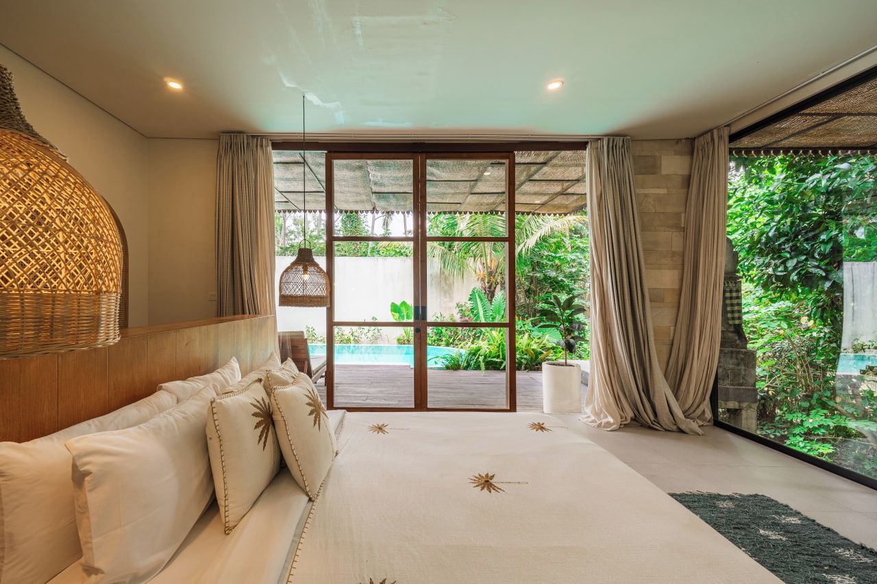 Quarto com cama grande, vista para um jardim e porta de vidro deslizante para área externa.