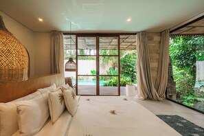 A bedroom with a large bed, a view of a garden, and a sliding glass door leading to an outdoor area. - Abangan Palace Ubud - Jungle View (Ubud)