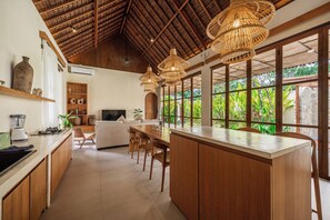 A spacious kitchen with a large island, wooden cabinets, and a dining area with a table and chairs. - Abangan Palace Ubud - Jungle View (Ubud)