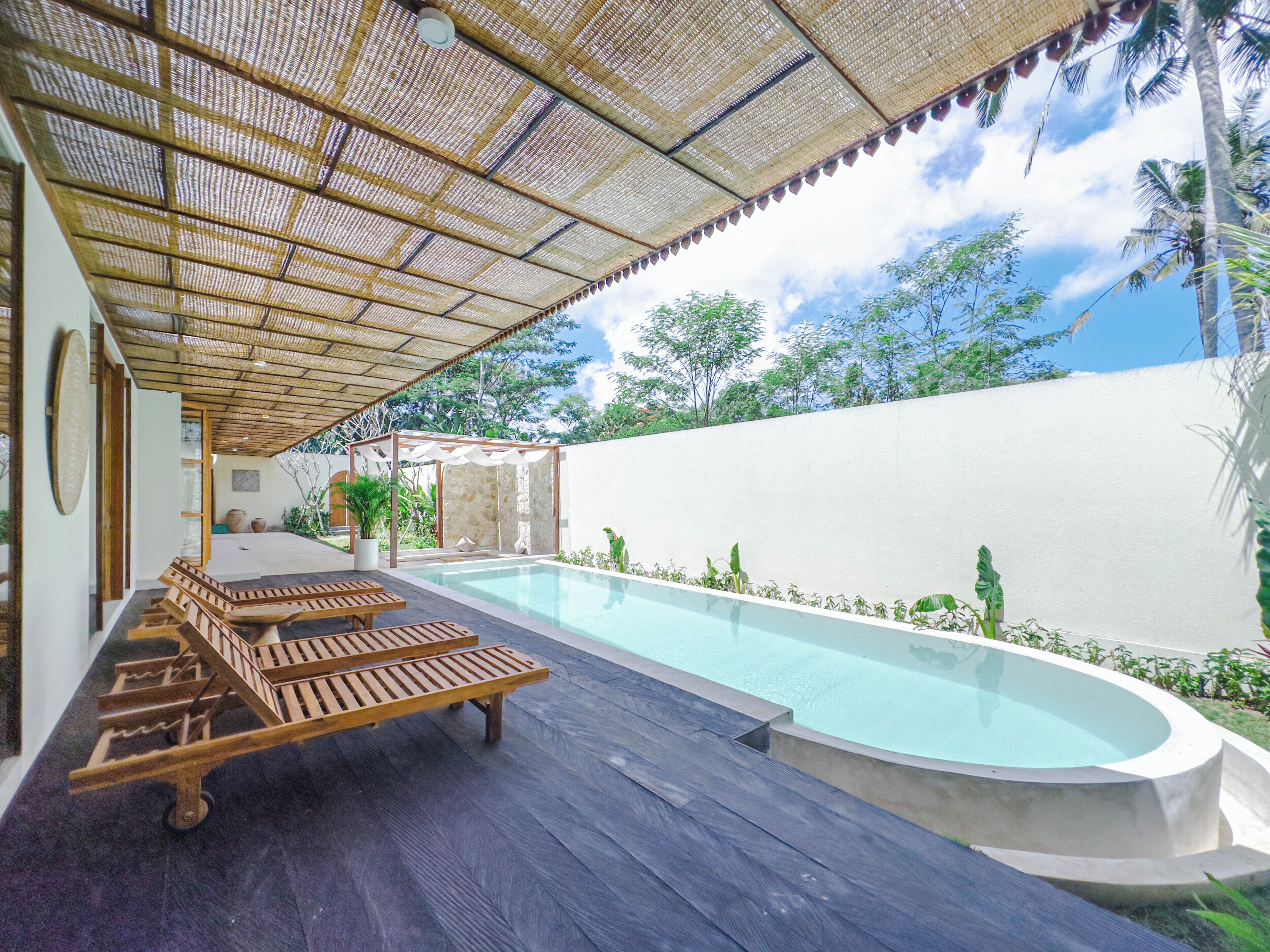 Un espace piscine avec des chaises longues en bois et une pergola.