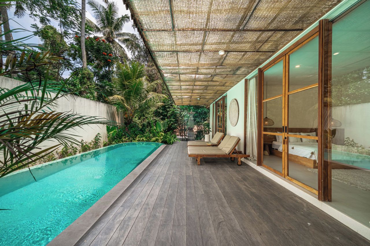 Área de piscina com deck de madeira, espreguiçadeiras e um espaço envidraçado.