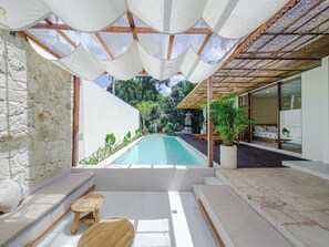 Un área de piscina exterior moderna con pared de piedra, asientos de madera y un porche cubierto.