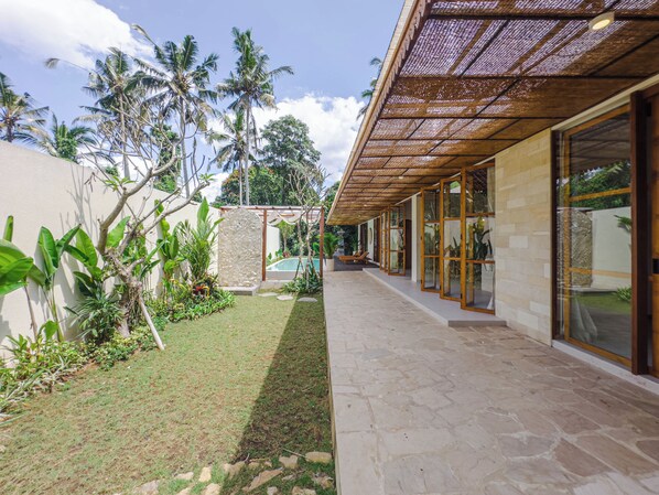 A covered outdoor area with a pool, stone flooring, and tropical plants. - Abangan Palace Ubud - Jungle View (Ubud)