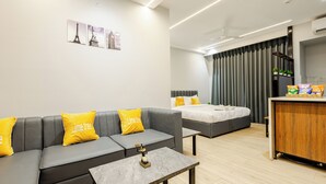 A modern hotel room with a grey sofa, a bed, a wooden desk, and a small table. - Street Studio by Lime Tree Hotels (Gurugram)