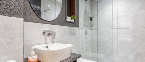 A modern bathroom with a white sink, a mirror, and a shower area.