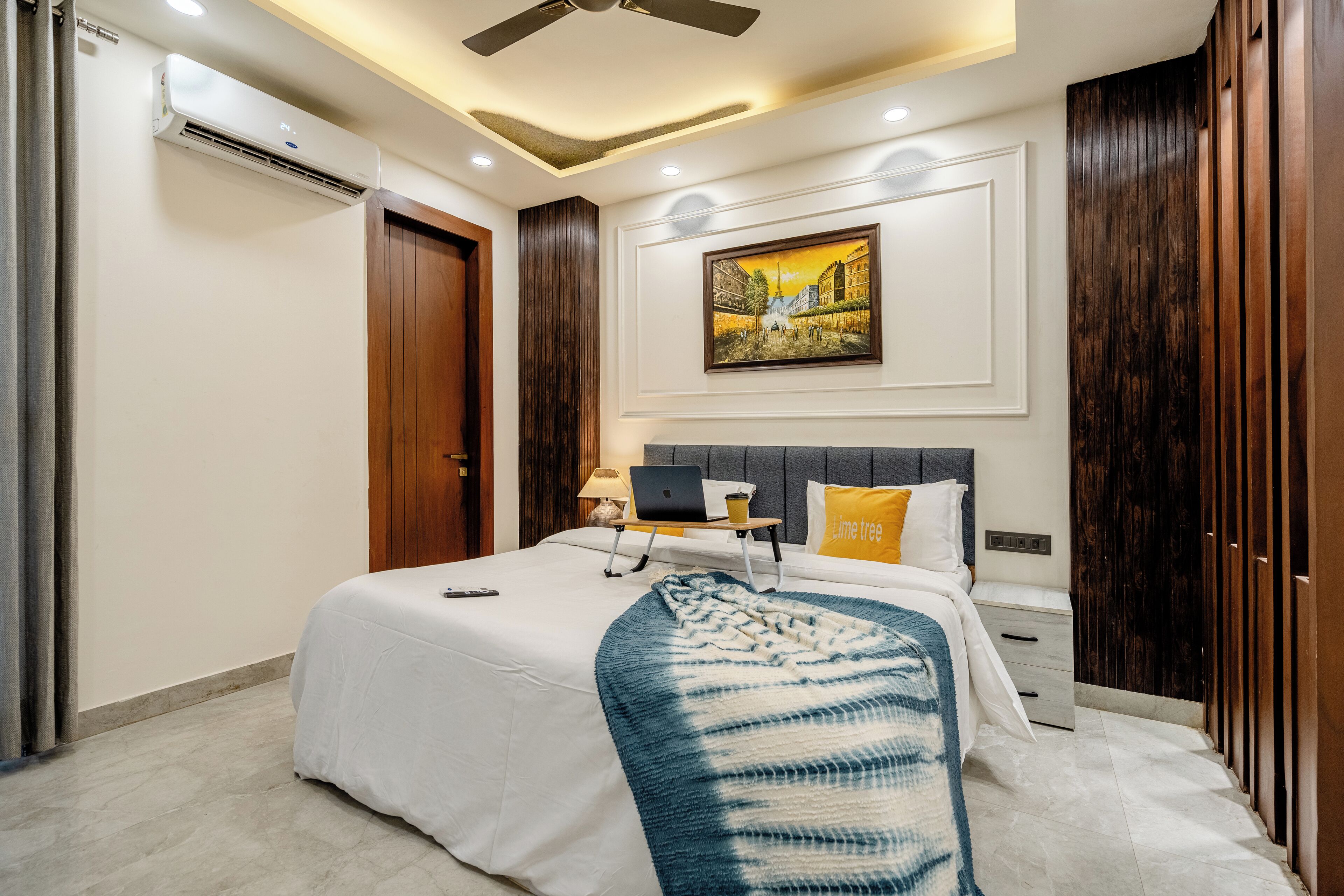 A modern bedroom with a bed, bedside table, lamp, laptop, and a painting on the wall.