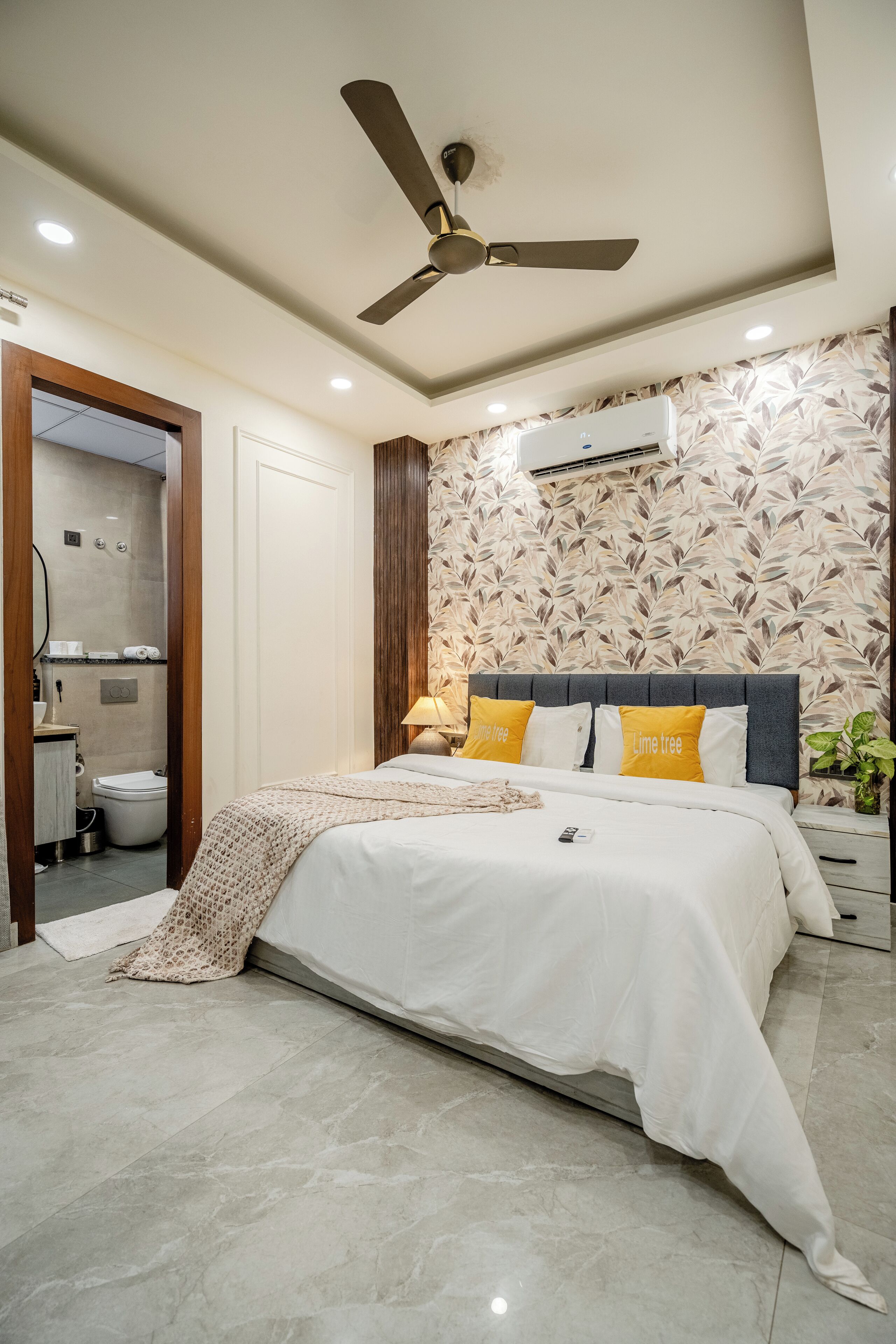 A bedroom with a bed, a ceiling fan, an air conditioning unit, and a bathroom visible through an open door.