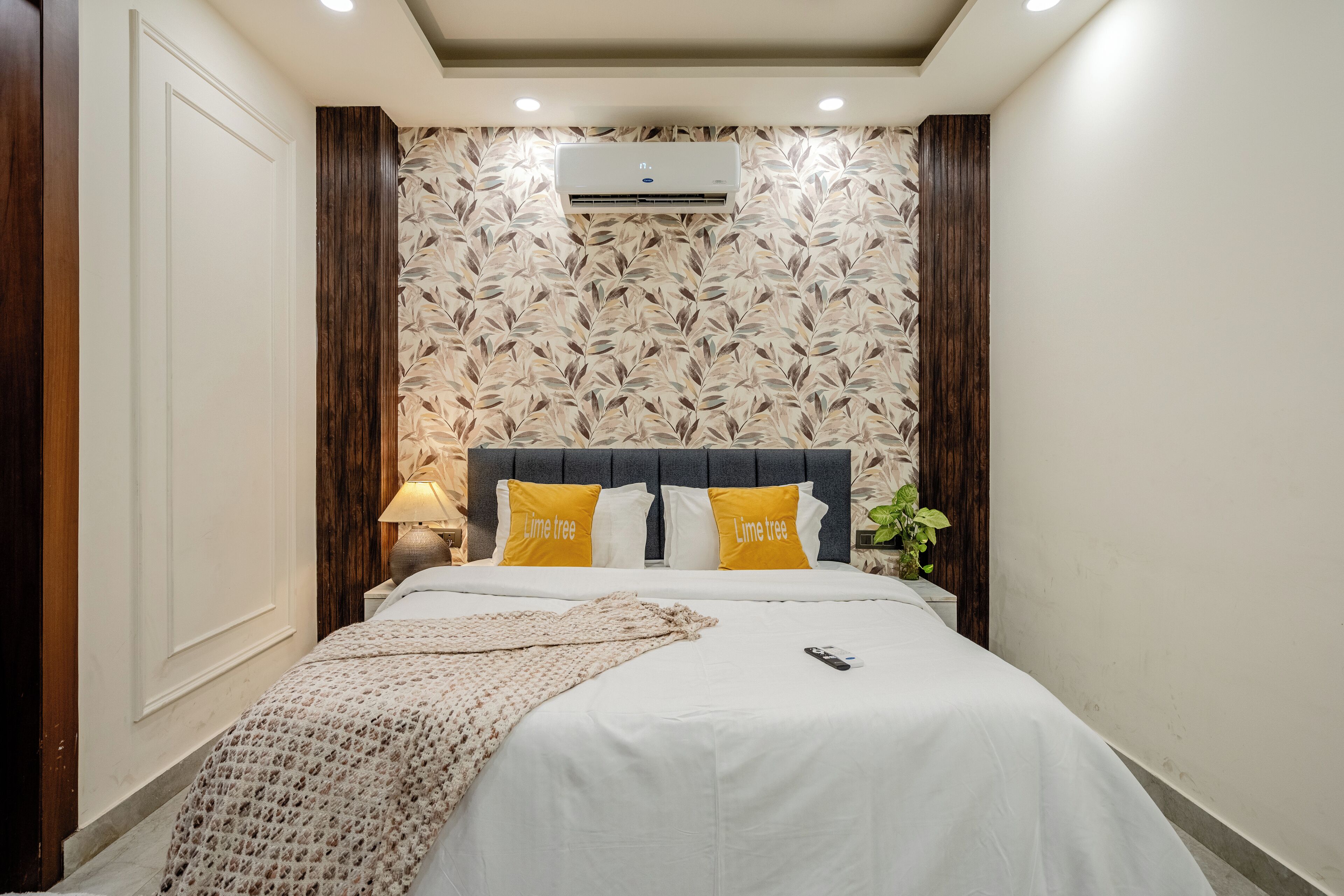 A neatly made bed with white bedding and two pillows labeled "Lime tree," a bedside lamp, and a wall-mounted air conditioner.
