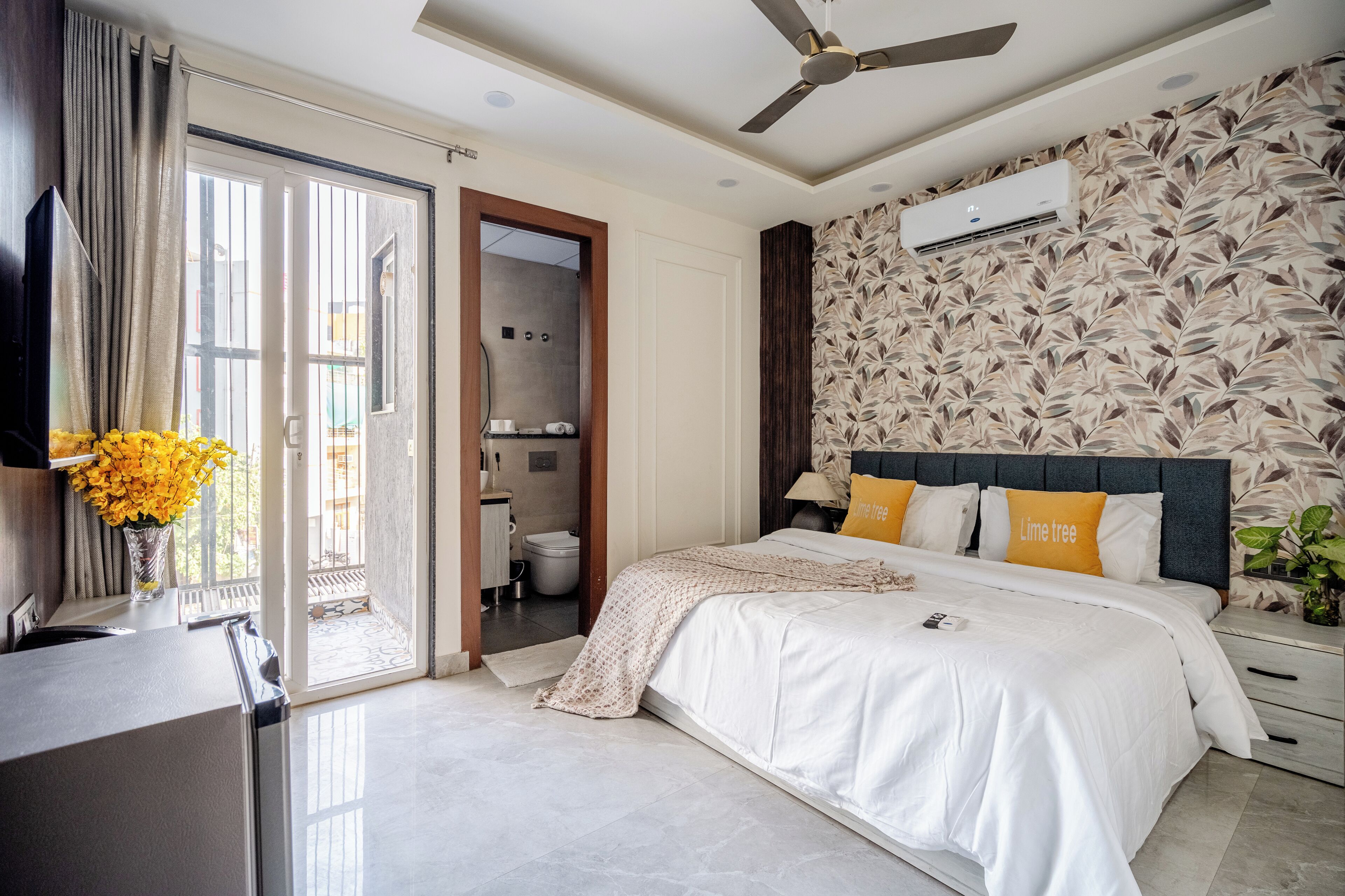 Un dormitorio con cama, ventilador de techo, aire acondicionado instalado en la pared y un baño visible a través de una puerta abierta.