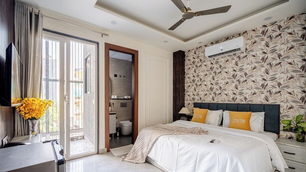 A bedroom with a bed, a ceiling fan, a wall-mounted air conditioner, and a bathroom visible through an open door. - Street Studio by Lime Tree Hotels (Gurugram)