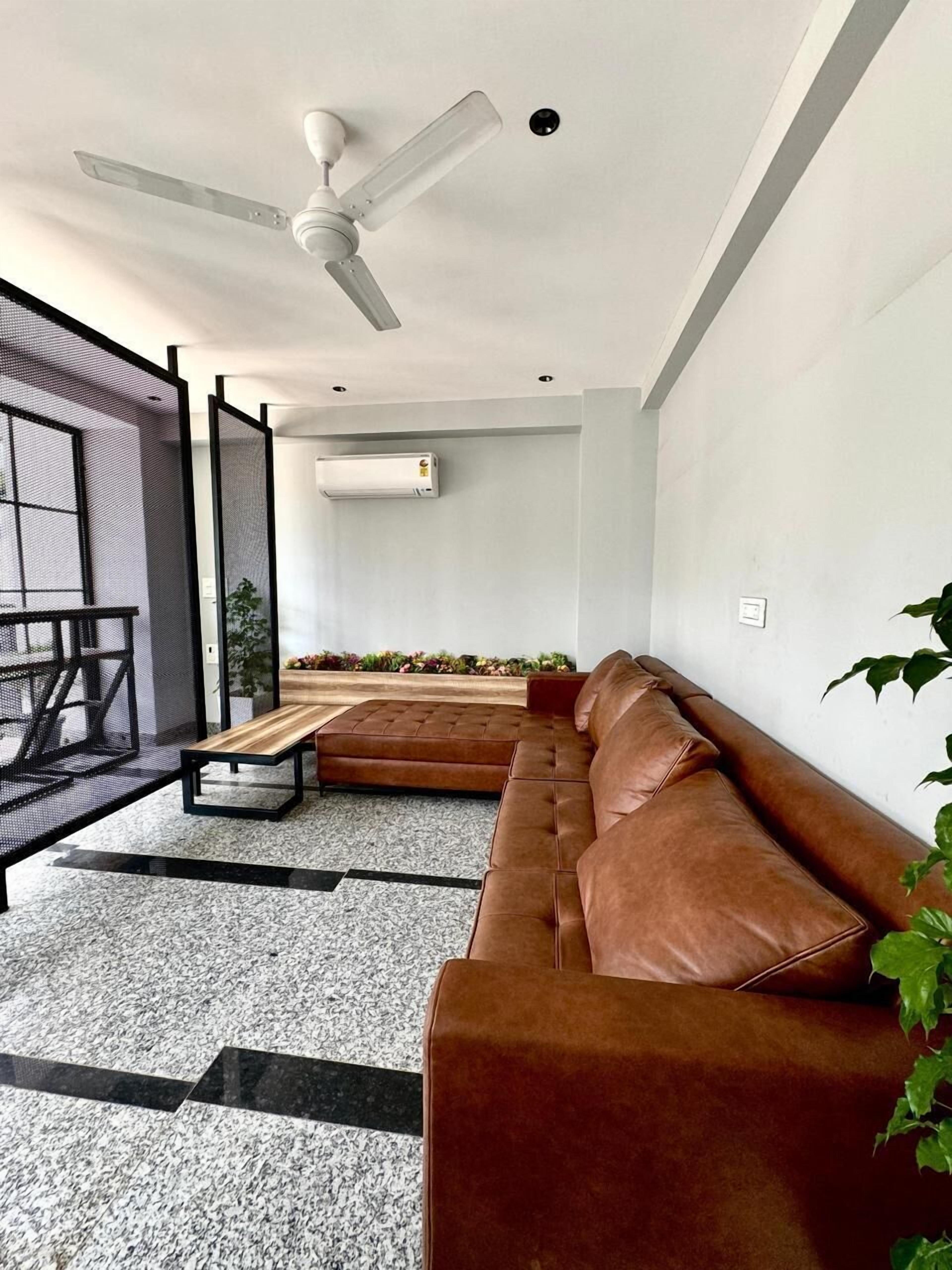 A modern living room with a brown leather sofa, a ceiling fan, and an air conditioning unit.