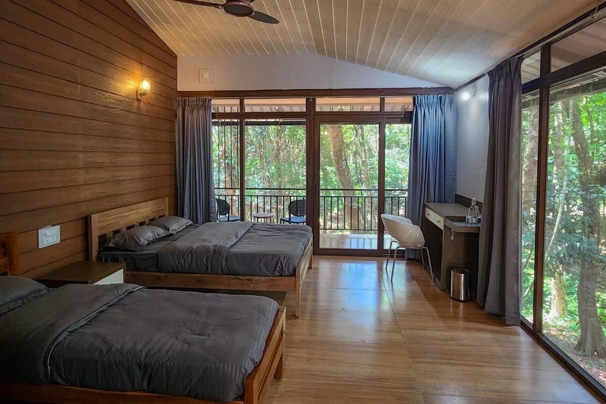Eine Hütte mit zwei Betten, einem Schreibtisch und großen Fenstern mit Blick auf einen Wald.