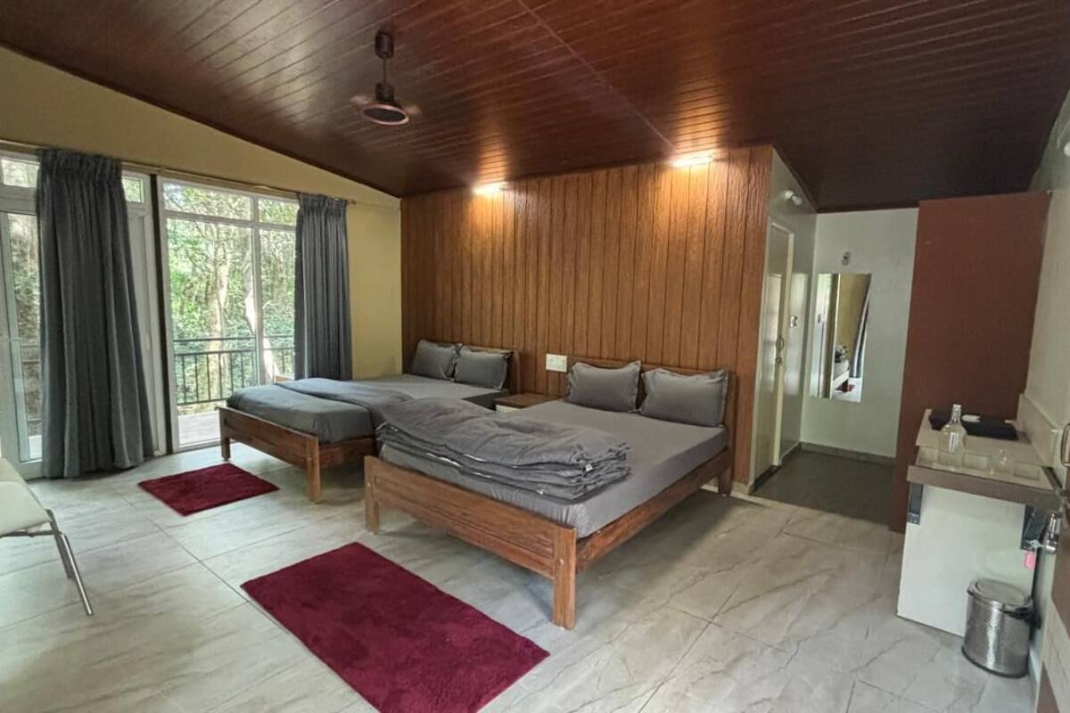 Ein Schlafzimmer mit einem großen Bett, Holzwandverkleidung, einer kleinen Küchenzeile und Blick ins Grüne durch die Fenster.