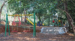 Kids can play on the swing set, slide, and climbing structure in this outdoor playground surrounded by trees.