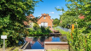 Een gracht met een houten brug, een bakstenen huis en een bord in een vreemde taal.
