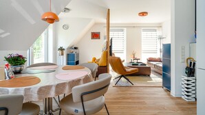 Een moderne keuken met een eethoek, met een ronde tafel met placemats, een hangende oranje hanglamp en uitzicht op de woonkamer.