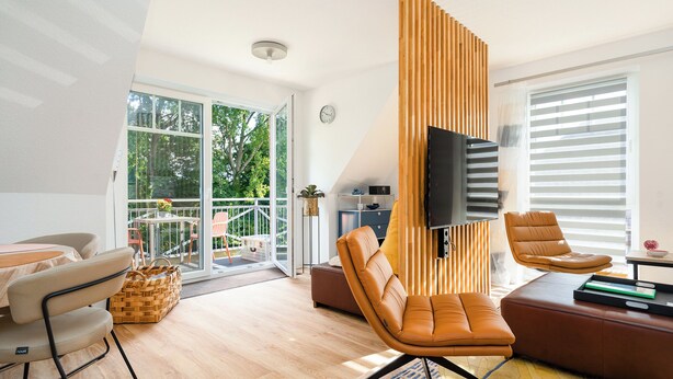 Een moderne woonkamer met een bank, stoelen, een televisie en een balkon met uitzicht op bomen.