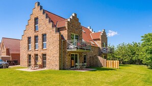 Een twee verdiepingen tellend, bakstenen huis met een balkon, een klein terras met tuinmeubilair en een verzorgd gazon.