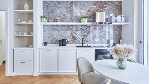 A modern kitchen with white cabinetry, a marble backsplash, and a dining area with a white table and chair.