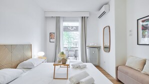 Une chambre d’hôtel comprenant un lit, une table de chevet avec une lampe, un canapé, une fenêtre avec des rideaux et un radiateur.