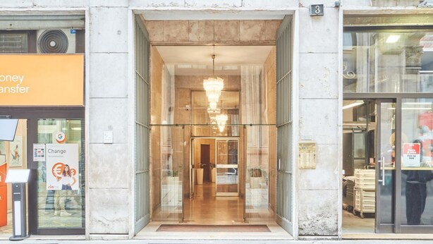 A hotel entrance with a glass door, a chandelier, and a visible interior through the glass. - Easylife - Refined apartment in Duomo (Milano)
