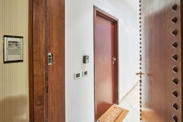 A hotel entrance with a wooden door, a doormat, and a wall-mounted intercom system.