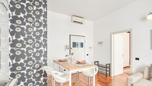A modern kitchen with a wooden table and white bar stools, a patterned wallpaper, and a visible door leading to another room. - Easylife - Refined apartment in Duomo (Milano)