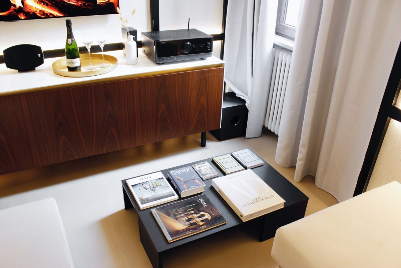 A modern living room with a wooden cabinet, a coffee table with books, a wine bottle, and glasses.
