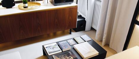 A modern living room with a wooden cabinet, a coffee table with books, a wine bottle, and glasses.