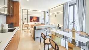A modern kitchen with a central island, a dining area with a glass table, and a large window with curtains.