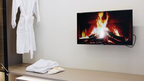 A modern bathroom with a flat-screen TV displaying a fireplace, a white robe, and slippers on the counter.