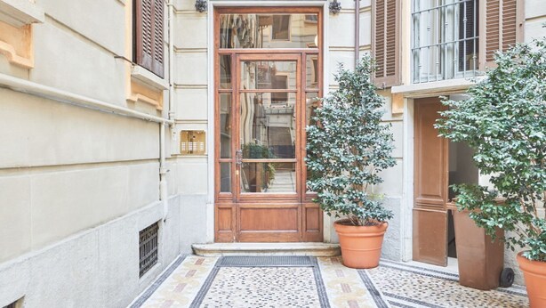 Une entrée d’immeuble avec une porte en bois, des plantes en pot et un sol recouvert de carreaux.
