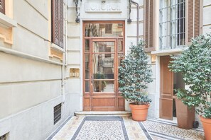 A building entrance with a wooden door, potted plants, and a tiled pavement.