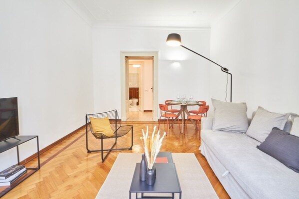 A modern living room with a sofa, a coffee table, a TV, and a dining area with chairs and a table.