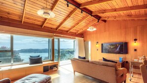 A modern living room with a large window, wooden ceiling, and a flat-screen TV.