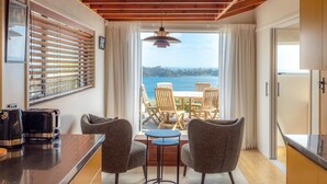 A modern kitchen with a view of the sea, wooden ceiling, and a dining area with chairs and a table.