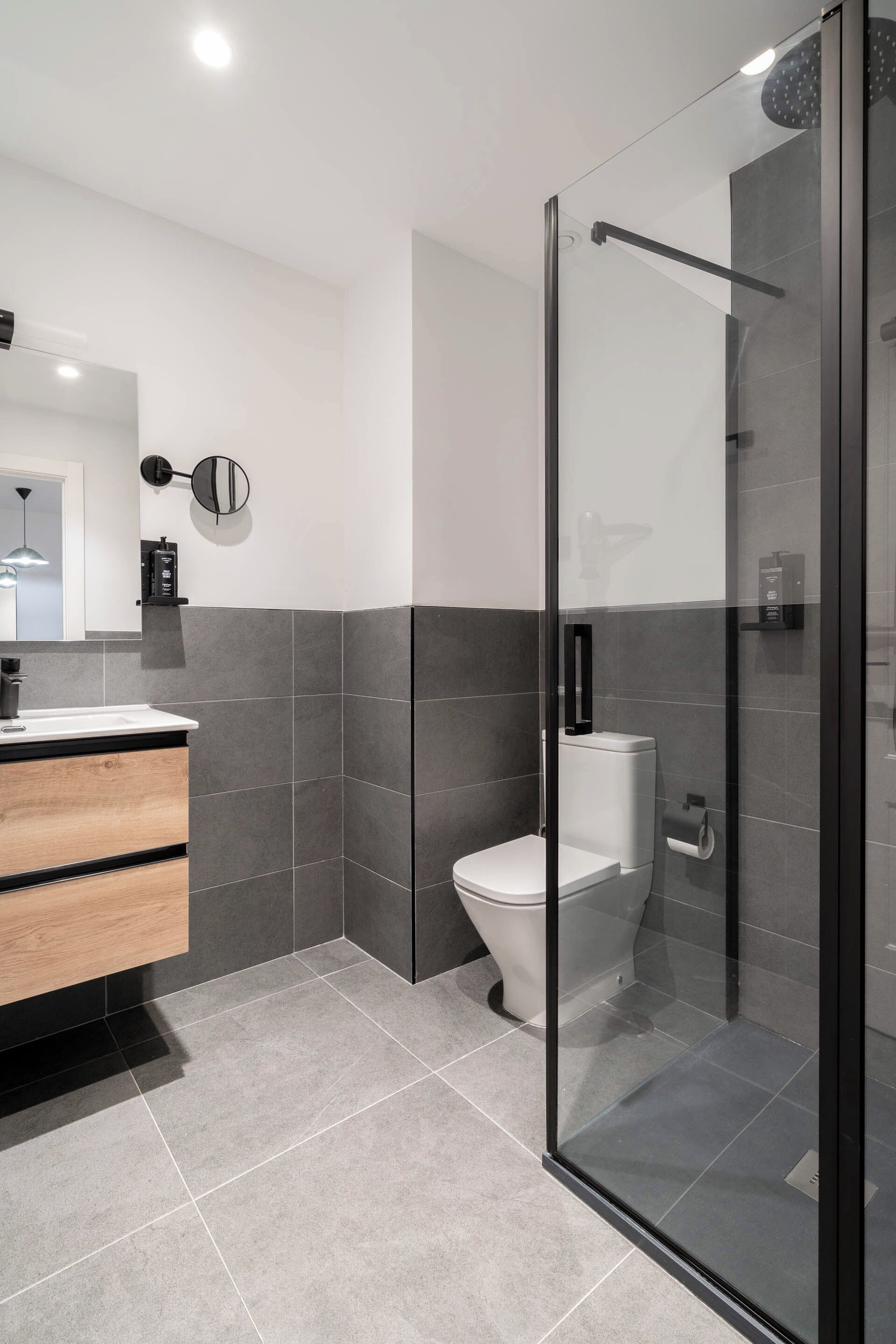 Un baño moderno con cabina de ducha de vidrio, tocador de madera y un inodoro.