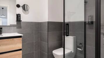 Un baño moderno con cabina de ducha de vidrio, tocador de madera y un inodoro.