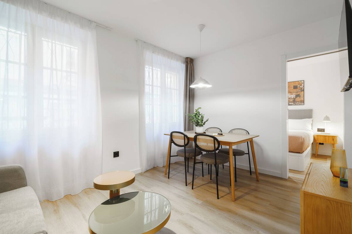 Ein stilvolles, helles Zimmer mit Essbereich, einem runden Tisch und einem Bett mit Nachttisch.