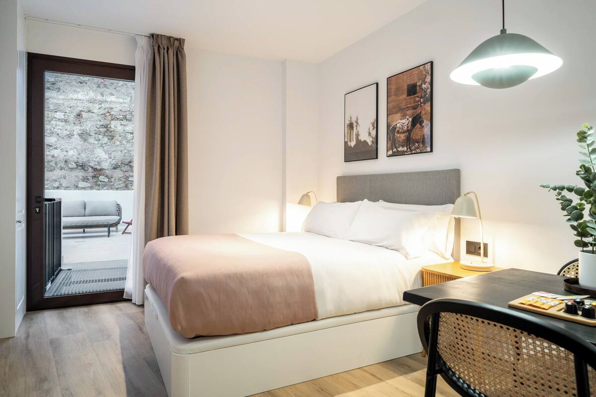 Ein Hotelzimmer mit Bett, Nachttisch, Lampe und Blick ins Freie.