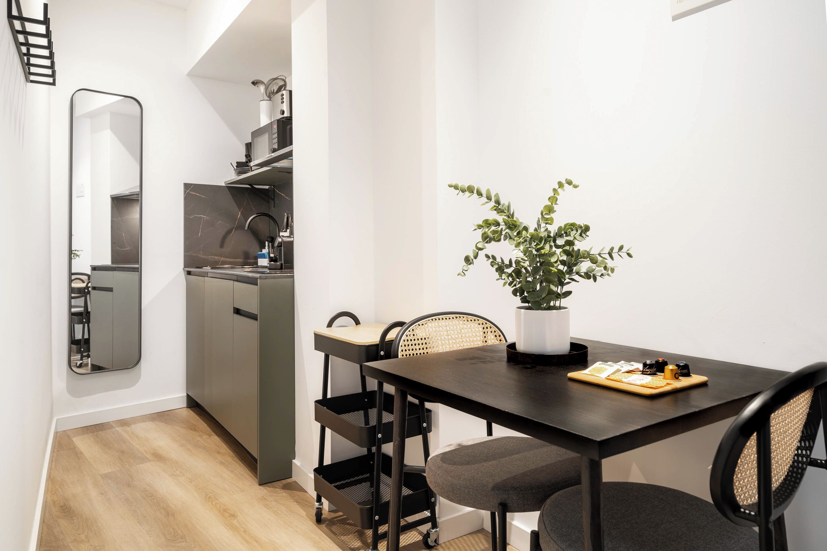 Une cuisine de taille réduite, dotée d’un plan de travail foncé, d’un évier et d’un petit coin repas avec une table et des chaises.