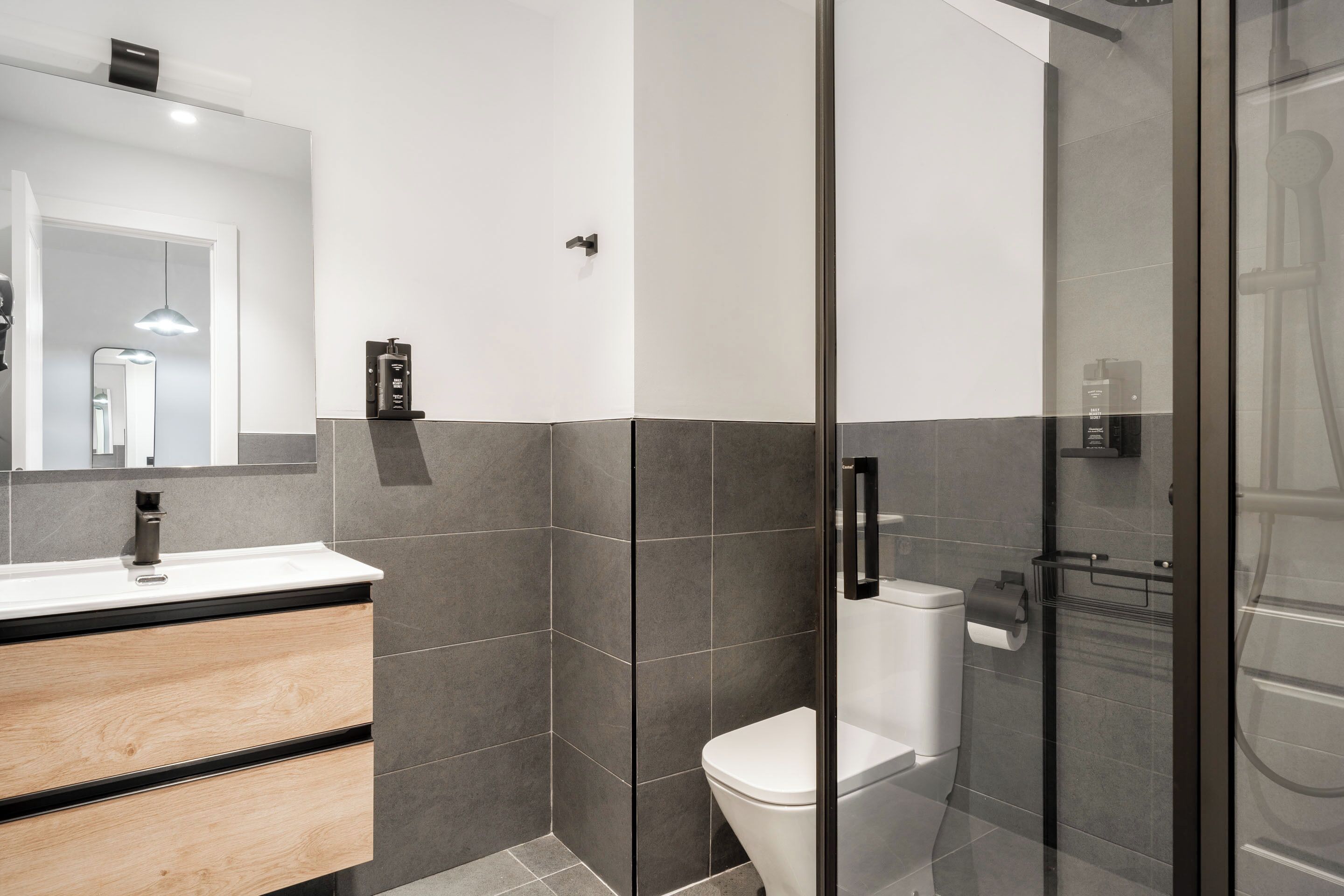 Een moderne badkamer met een douchecabine van glas, een wit toilet en een houten wastafelmeubel met een zwarte kraan.