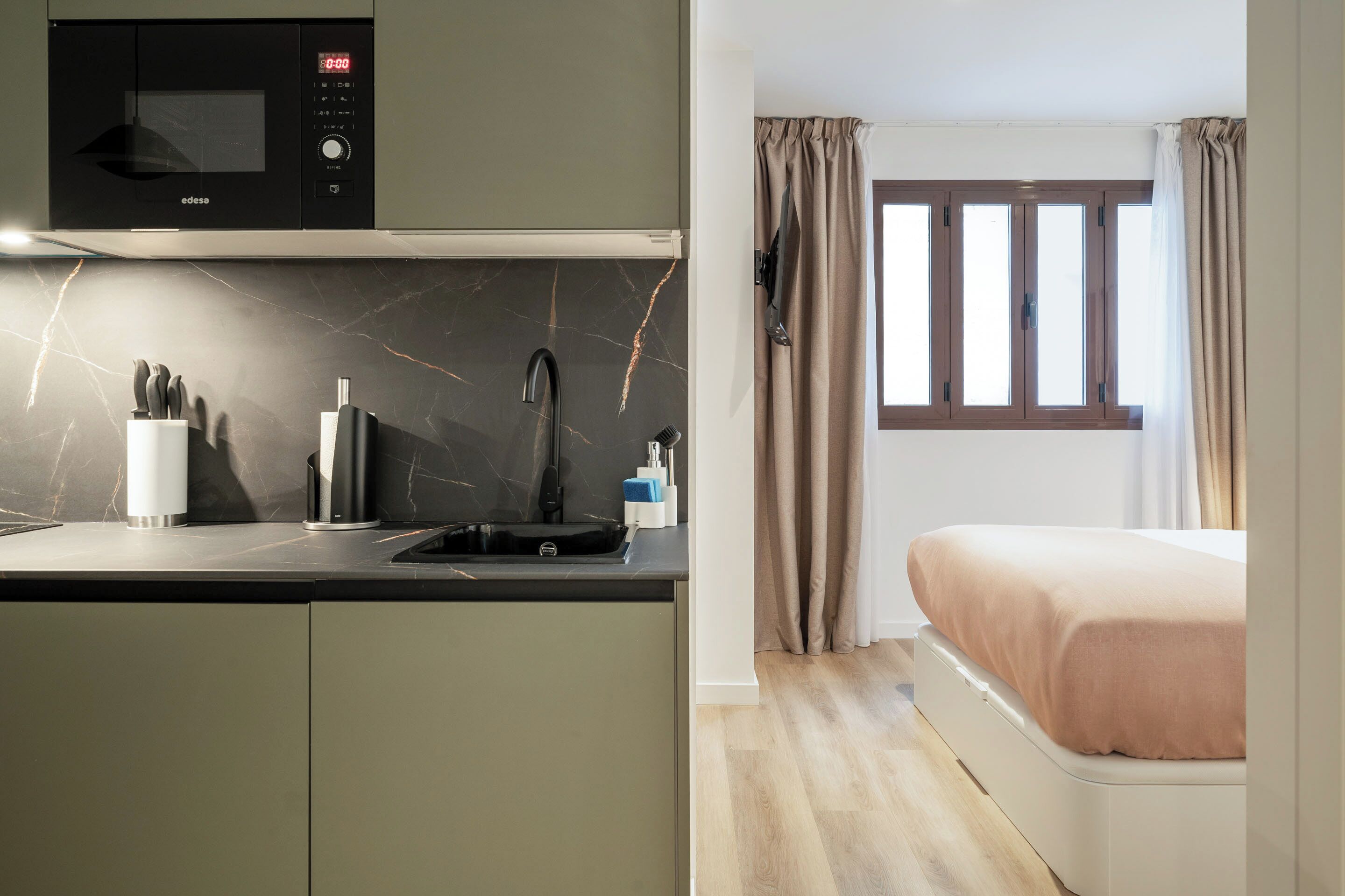 Cocina moderna con microondas, lavamanos y utensilios, además de un dormitorio con cama y ventana.