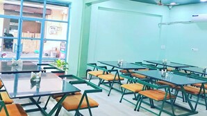 A conference room with green tables and orange chairs, large windows, and ceiling fans. - Hotel Sunrise Palace Udaipur (Udaipur)