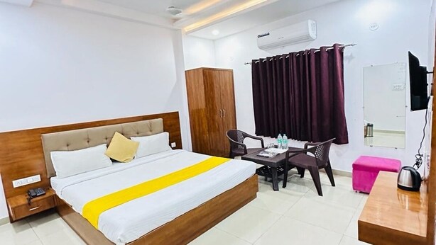 A hotel room with a bed, a desk, a chair, a wardrobe, a trash bin, and a mirror. - Hotel Sunrise Palace Udaipur (Udaipur)