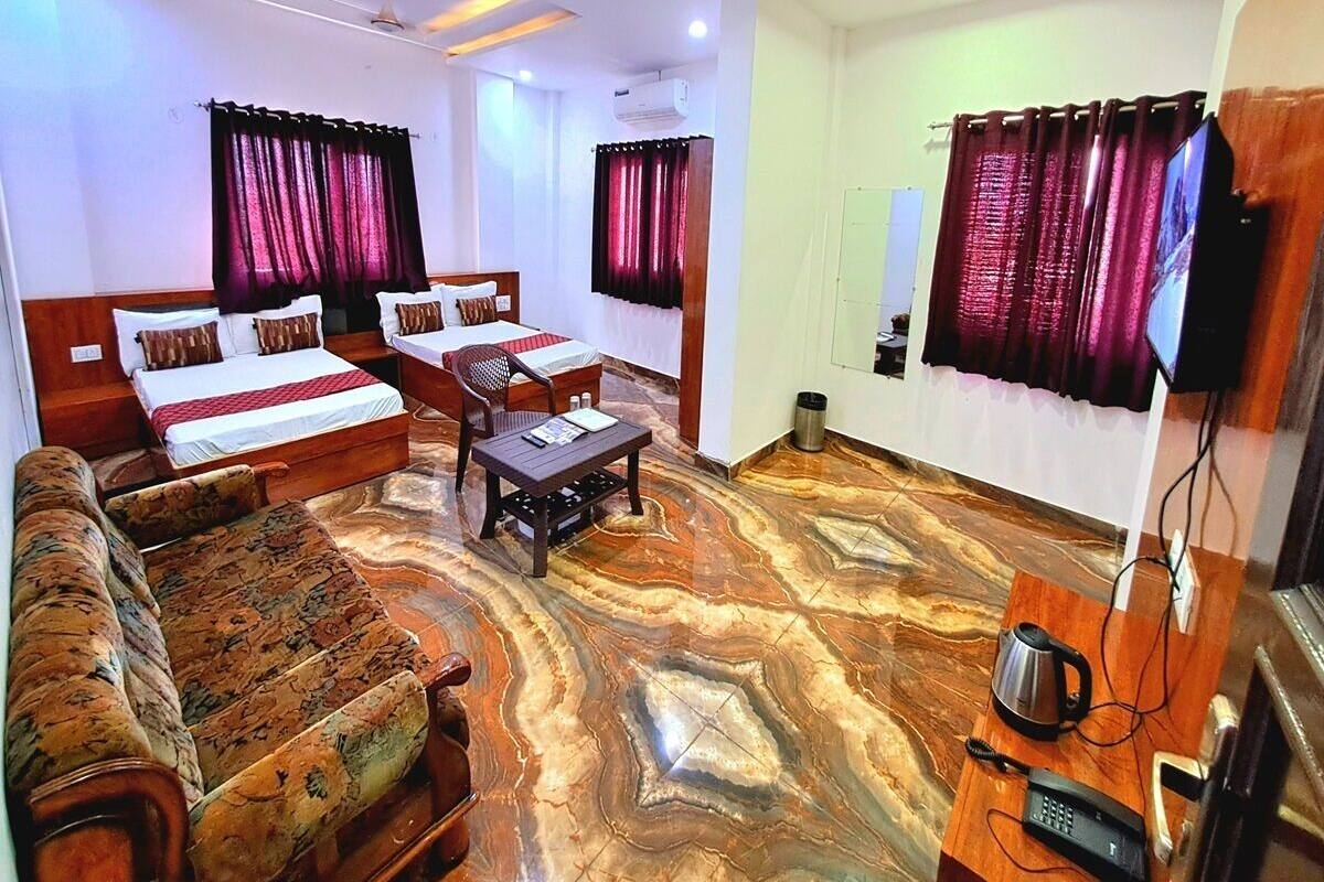 A hotel room with a bed, sofa, and a small table. There is a television mounted on the wall and a ceiling fan.