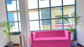 A room with a pink sofa, wooden flooring, and large windows with a view of buildings outside. - Hotel Sunrise Palace Udaipur (Udaipur)