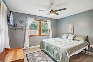 A bedroom with a bed, a ceiling fan, a TV, and a window with curtains. - Fawn Lake Cottage for Families Looking for Privacy (Wisconsin Dells)